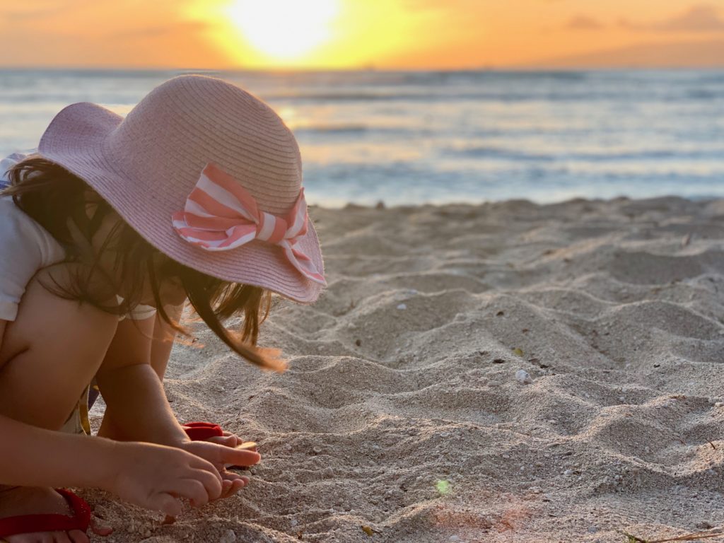 クイーンズビーチで夕日を背景に砂遊びをする娘