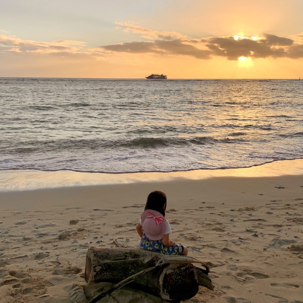 夕日と船と流木に座る娘